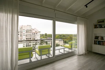 Balcón moderno con sillones verdes y vista urbana — proyecto Obra Segui M A, por Arq. Lourdes Yarade Saravia, en Buenos Aires
